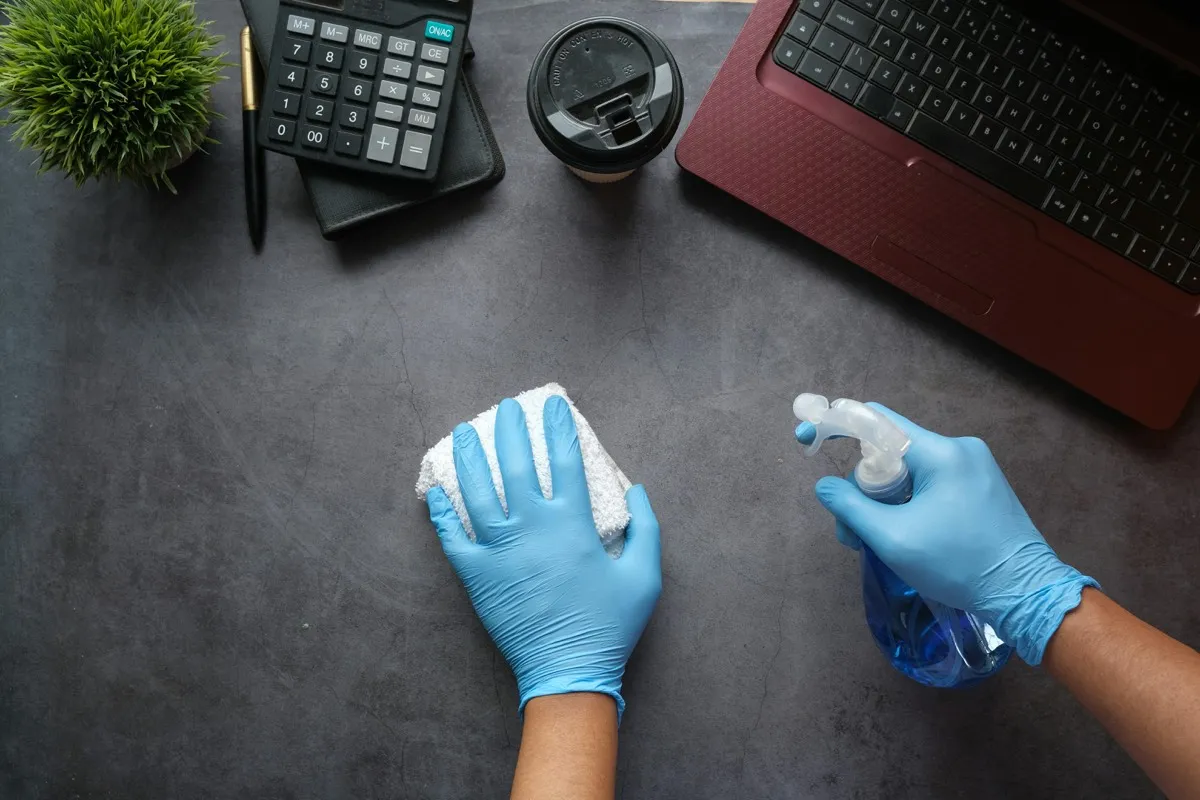 Professional cleaner with blue gloves sanitizing an office desk