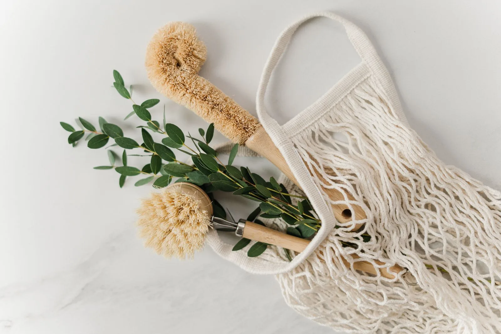 Wooden cleaning brushes and eucalyptus sprigs in a cotton mesh bag.