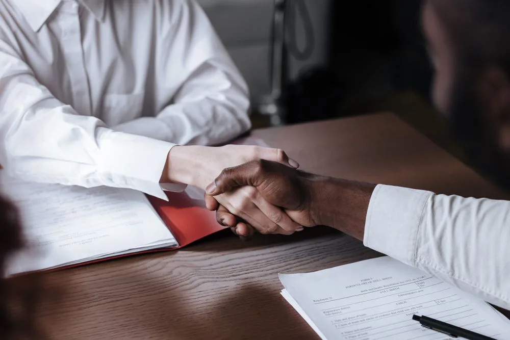 A handshake over documents at a desk, closing an agreement.