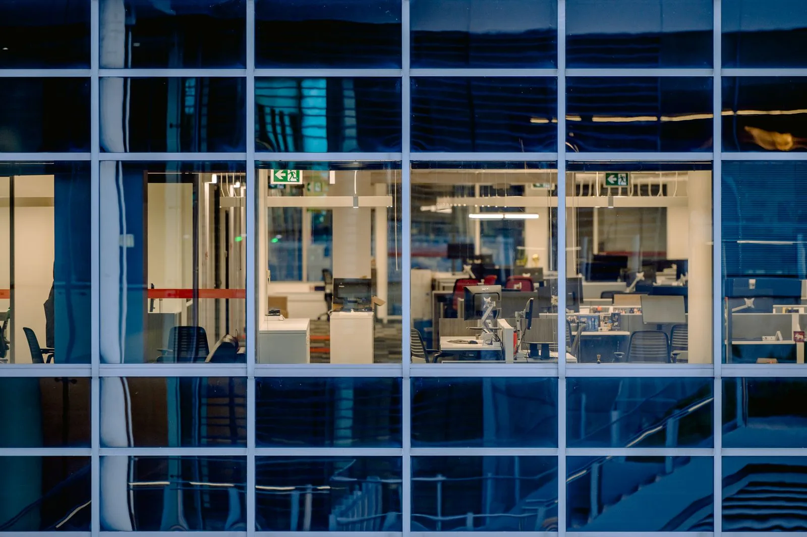 An office interior glowing through a glass facade at dusk.