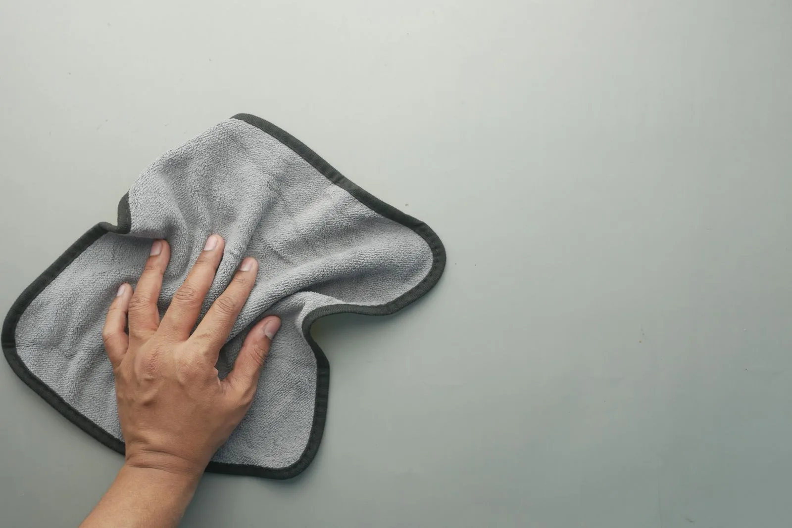 A hand wiping a surface clean with a grey microfiber cloth.