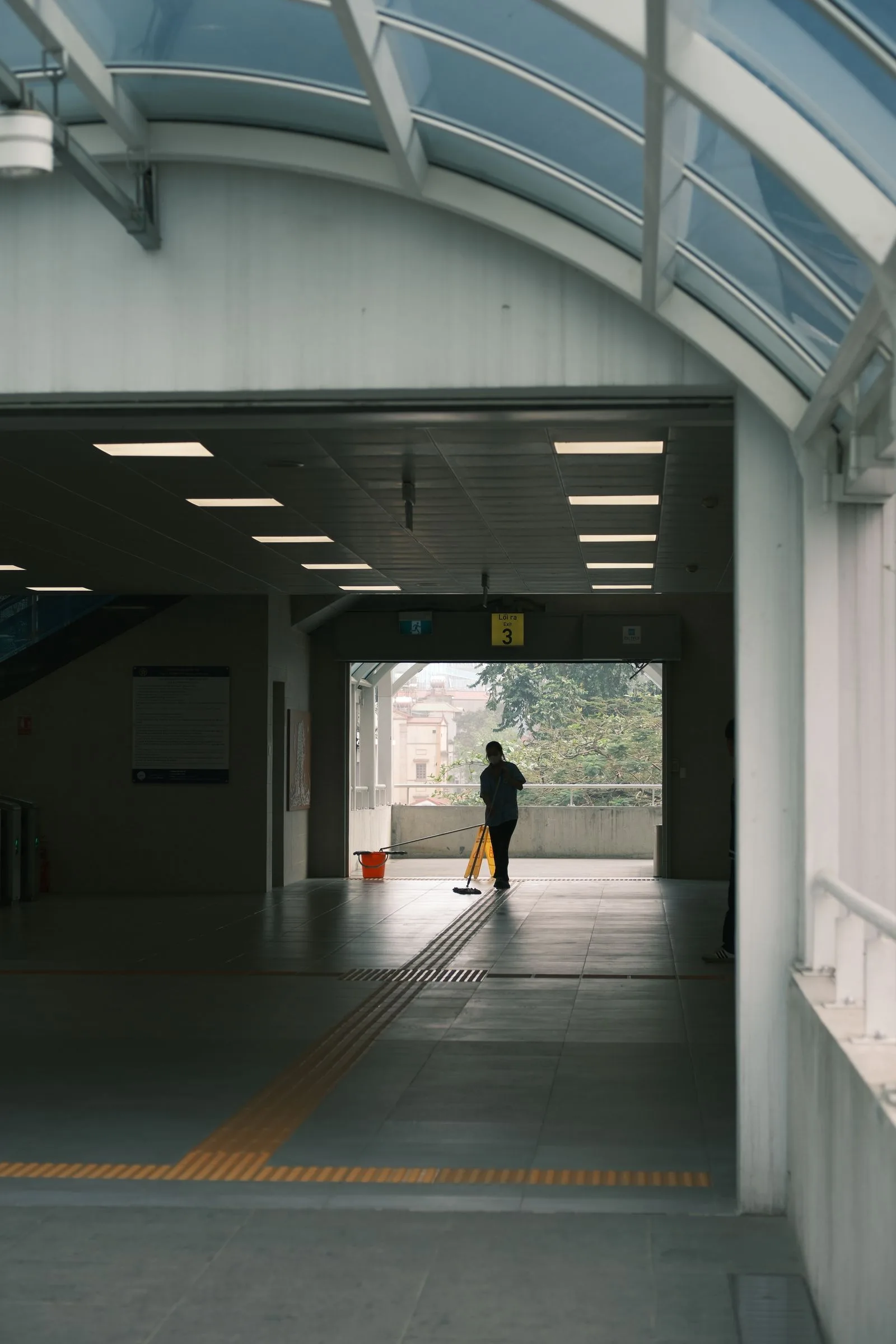 A lone cleaner maintaining a quiet transit passage in the evening.