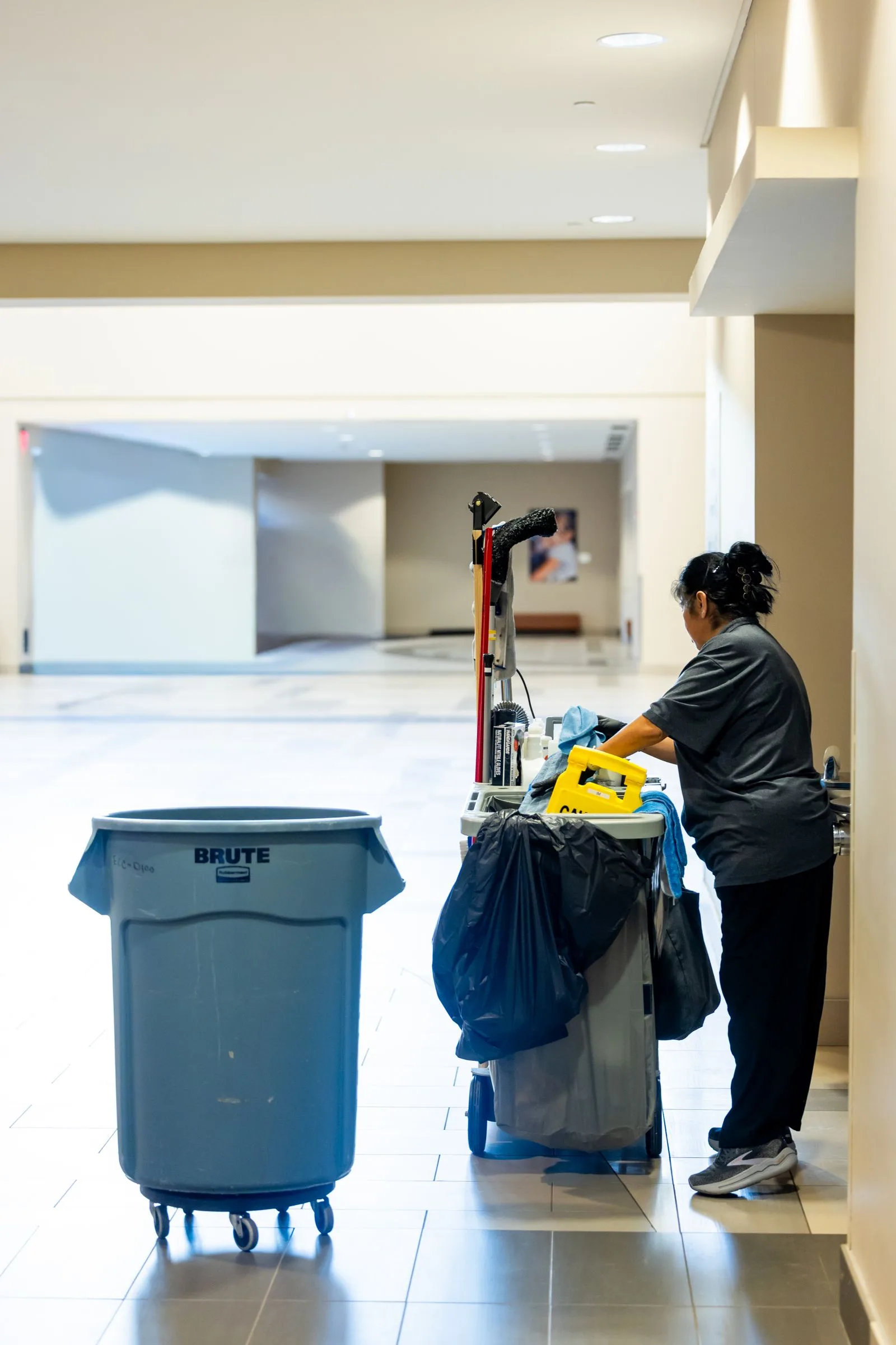 A cleaning professional with a service cart in a bright commercial atrium.
