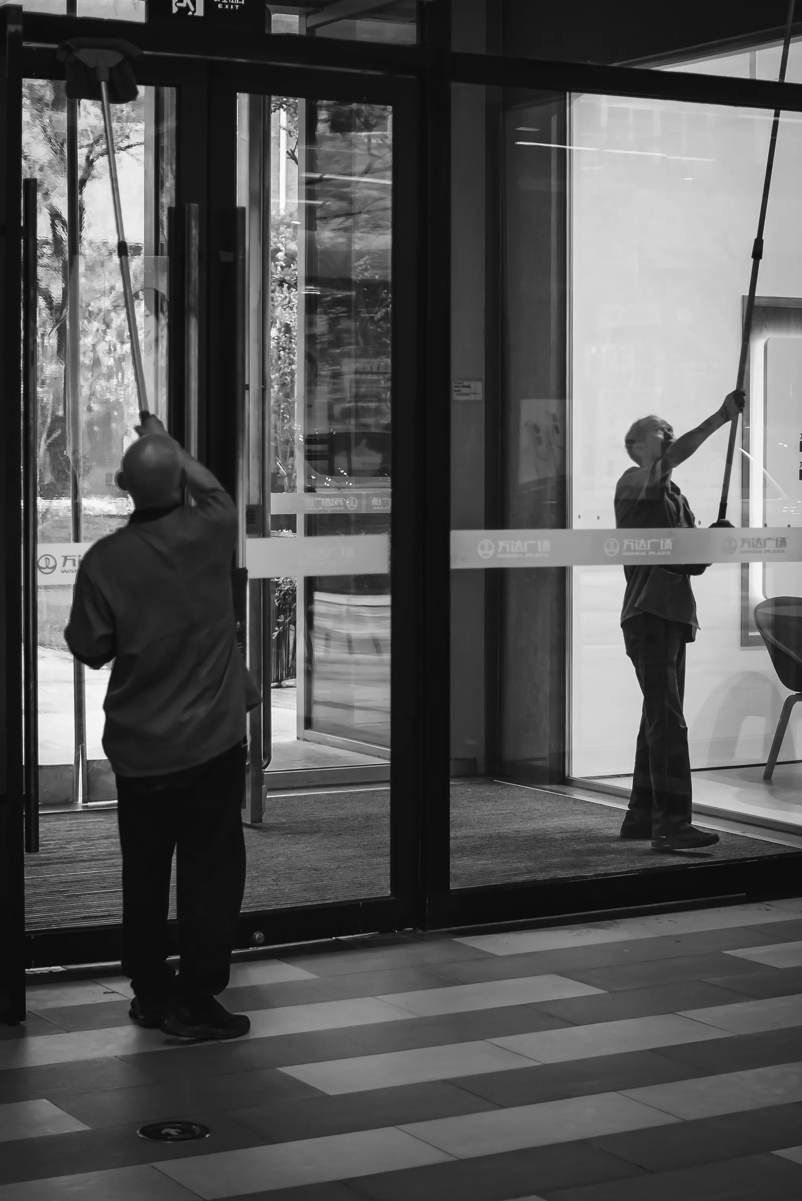 A cleaner squeegeeing the glass entrance of a commercial building.