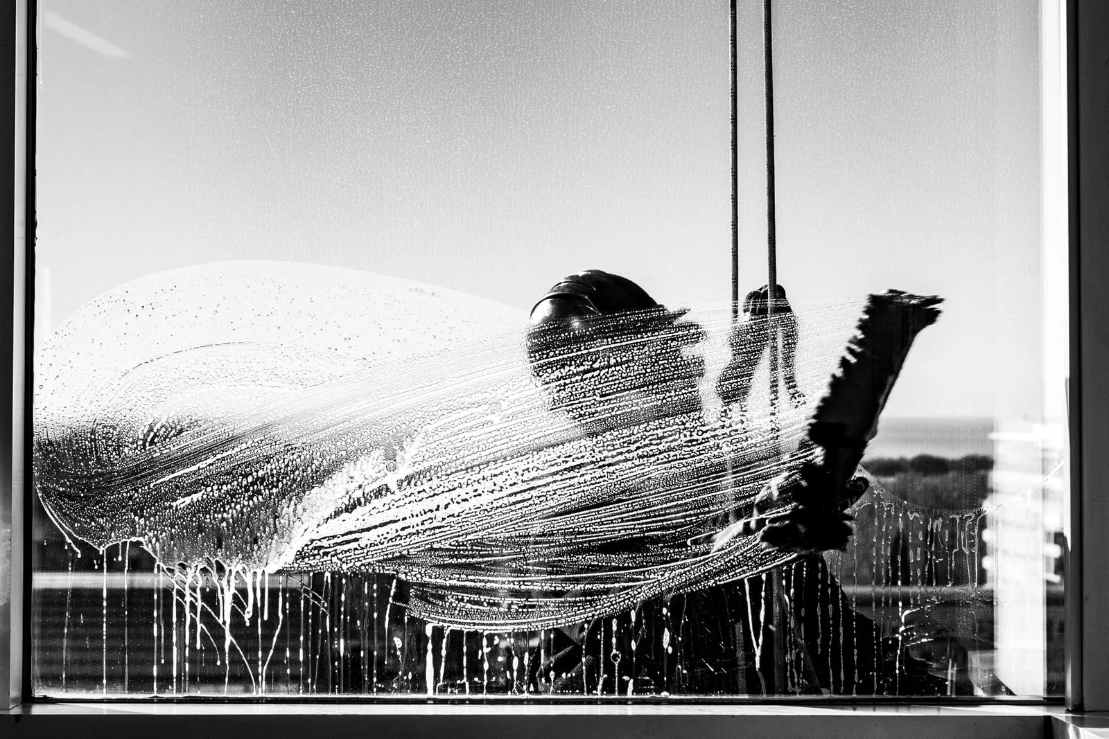An Ecco professional squeegeeing a soapy window clean with eco-certified products.