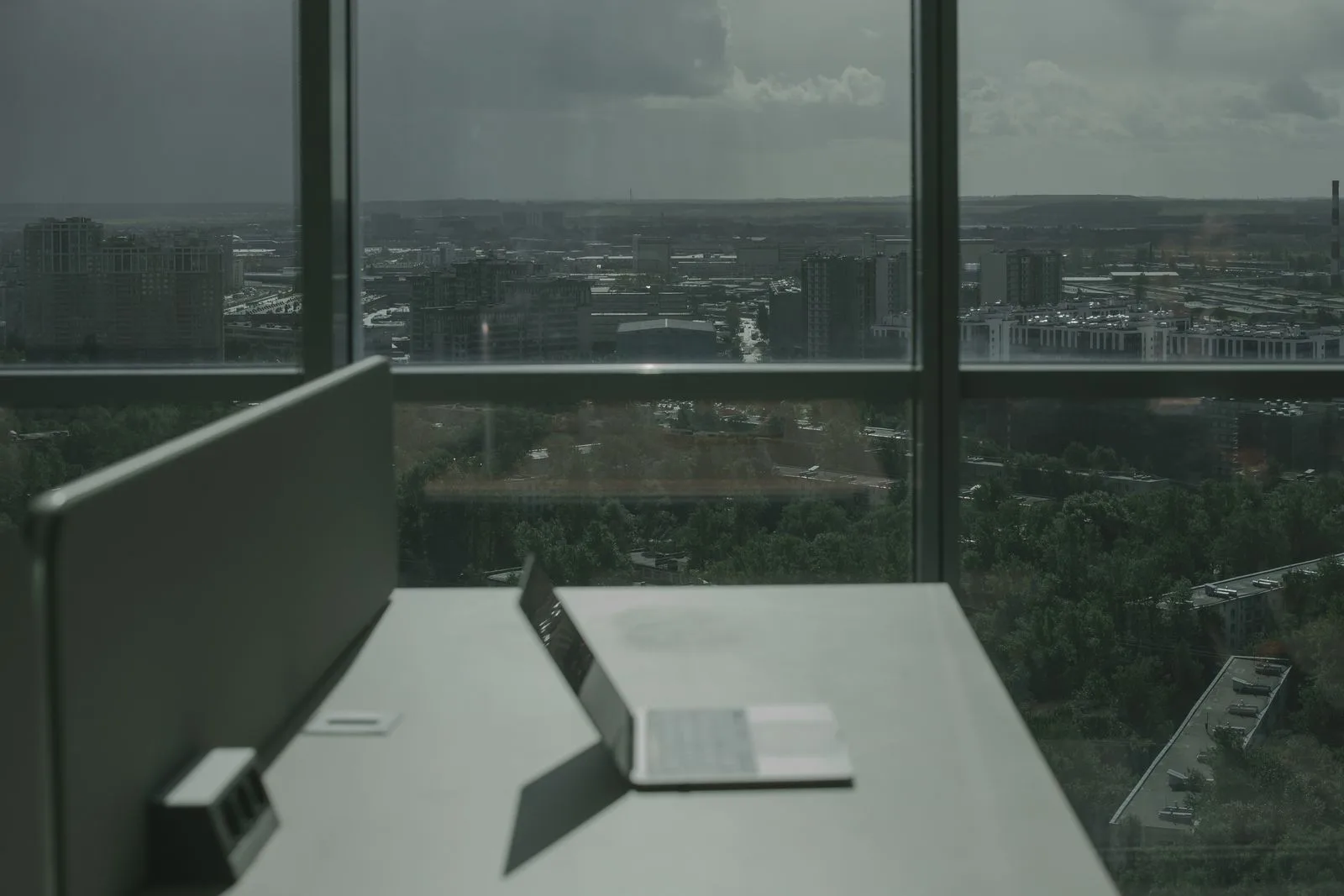 A tidy desk by floor-to-ceiling office windows overlooking the city at dusk.